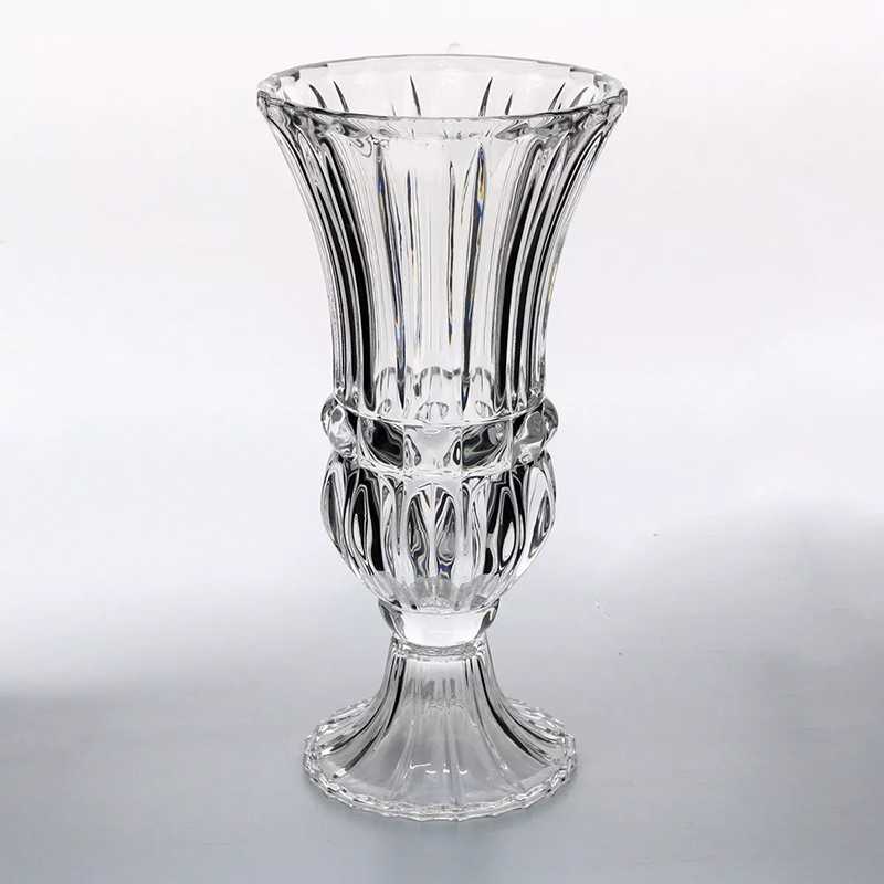 An exquisitely designed glass vase by *Basketeer*, showcasing a timeless blend of smooth and textured surfaces. The wide, flared rim gracefully descends into intricate vertical ridges along its tapered body, culminating in a rounded, ornamental base with an elegant pedestal-style foot. Positioned tastefully within a luxurious setting, the vase exudes classic sophistication. A delicate ribbon adorned with the *Basketeer* logo enhances its inviting allure.

