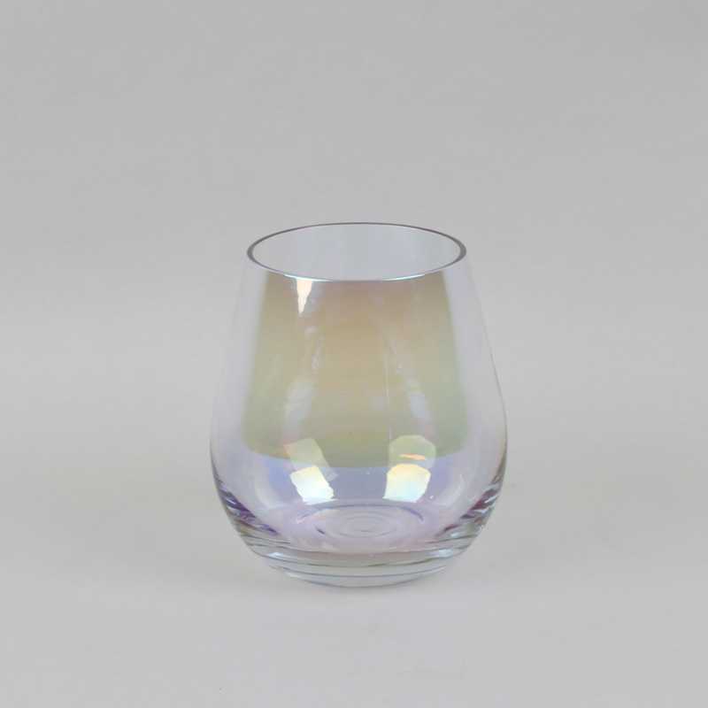 An exquisite clear glass tumbler from Basketeer, showcasing a subtle iridescent sheen, graces a minimalist light grey background. The glass boasts a sophisticated rounded and slightly tapered silhouette that elegantly widens towards the top, capturing and reflecting light in a gentle spectrum of luxurious colors. A promise of refined taste and understated elegance encapsulated by the renowned Basketeer brand.