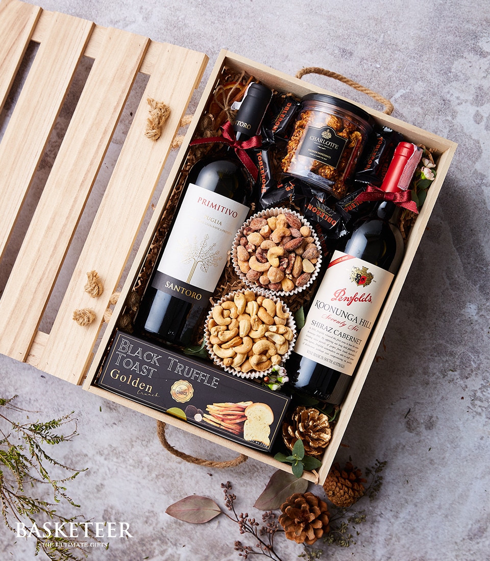 A lavish wooden gift box by Basketeer, adorned with a tasteful ribbon bearing the brand's elegant logo. This exquisite collection features two bottles of fine wine—Primitivo Santoro and Penfolds Koonunga Hill—nestled alongside a jar of gourmet preserves. The indulgence continues with two luscious cupcakes brimming with mixed nuts, complemented by delicate Black Truffle Toast and a pack of artisanal jelly candies. To complete this luxurious offering, a charming small succulent sits gracefully on the side, adding a touch of nature's beauty to this opulent ensemble.