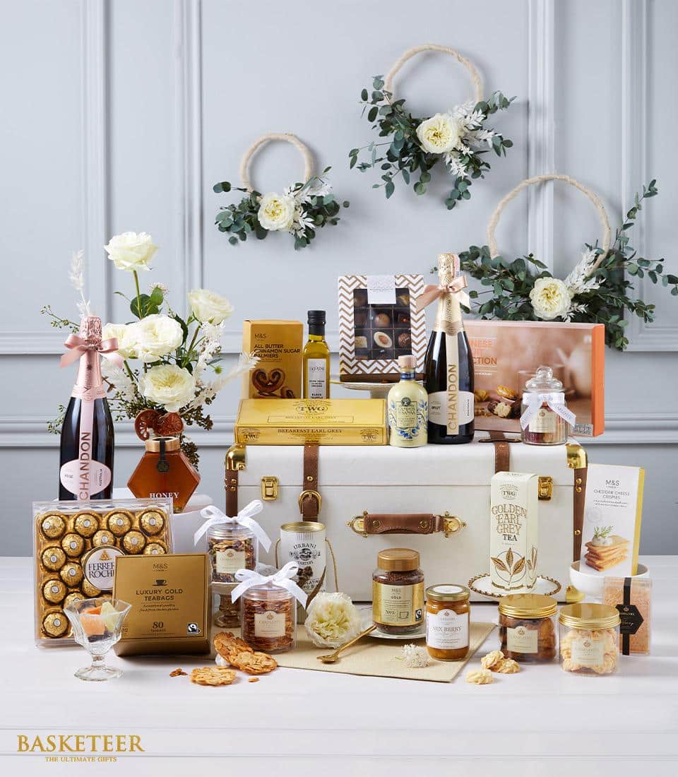 Immerse yourself in the sumptuous delights of the Gourmet Wine Delight Hamper by Basketeer. This opulent arrangement showcases an exquisite selection of chocolates, delectable jams, golden honey, and a bottle of sparkling wine. Elegantly presented on a sophisticated leather trunk and surrounded by lush flowers and greenery, the scene exudes luxury. The distinguished 