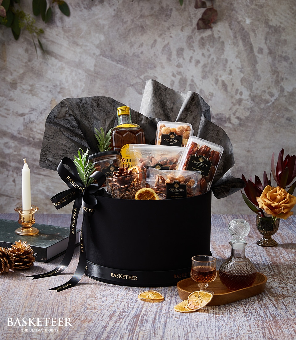 A premium black Charlotte hamper, brimming with nuts, dried fruit, liqueur and gourmet snacks, is styled with elegant gold accents.