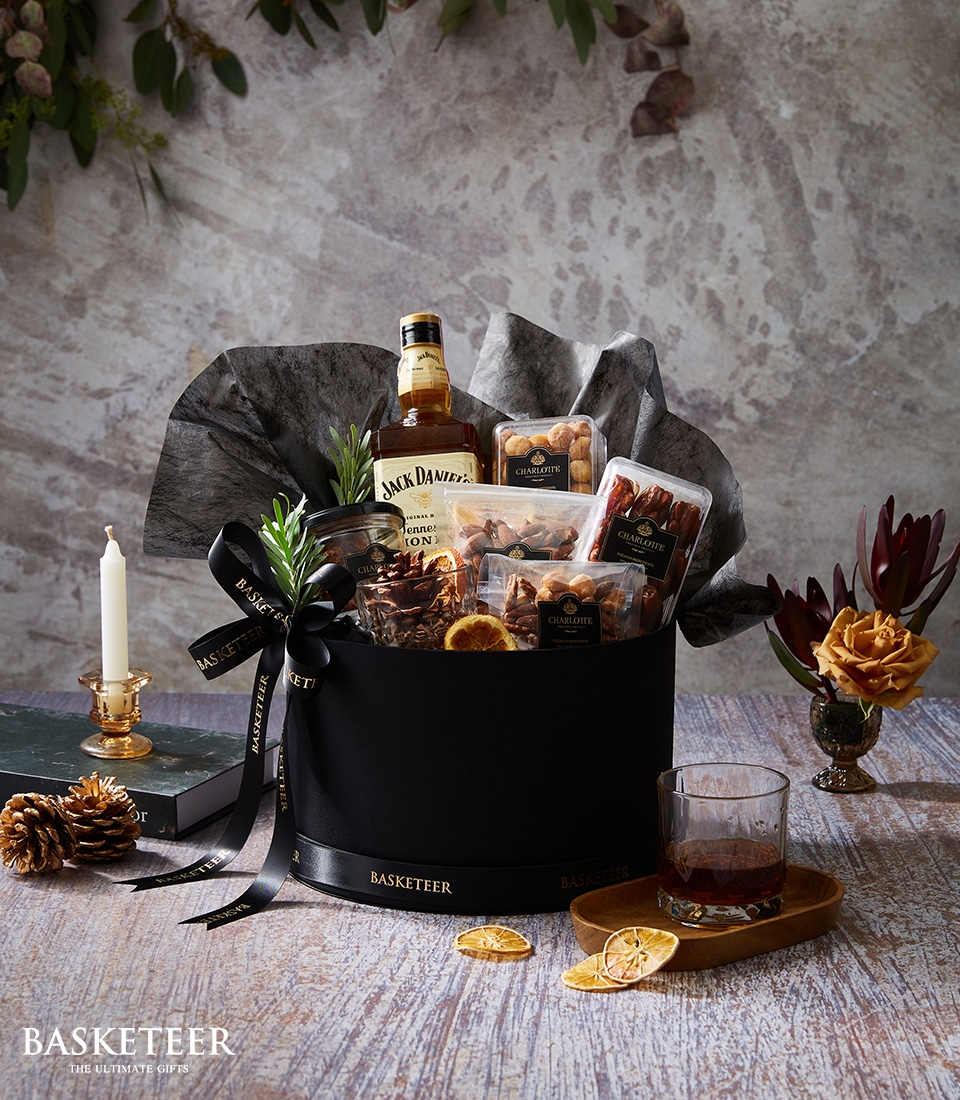A lavish gift basket featuring a premium bottle of Jack Daniel's whiskey, an array of gourmet chocolates, artisanal nuts, fragrant candles, and delectable dried fruits, all exquisitely presented in a sleek black container adorned with the elegant 