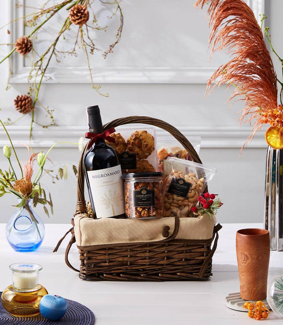 A beautifully curated wine and gourmet basket featuring a bottle of Negroamaro wine, assorted nuts, and premium snacks, elegantly presented in a rustic woven basket.