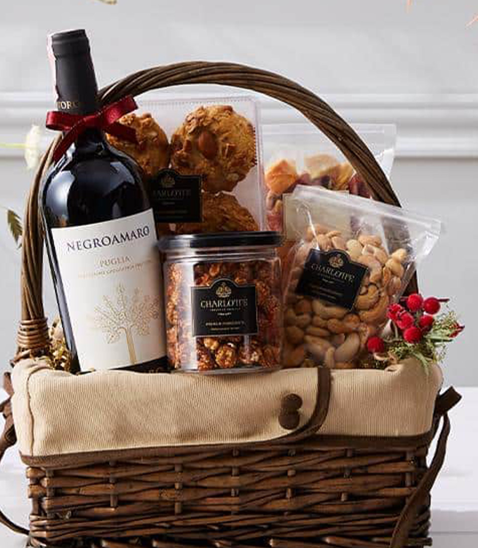 A beautifully curated wine and gourmet basket featuring a bottle of Negroamaro wine, assorted nuts, and premium snacks, elegantly presented in a rustic woven basket.