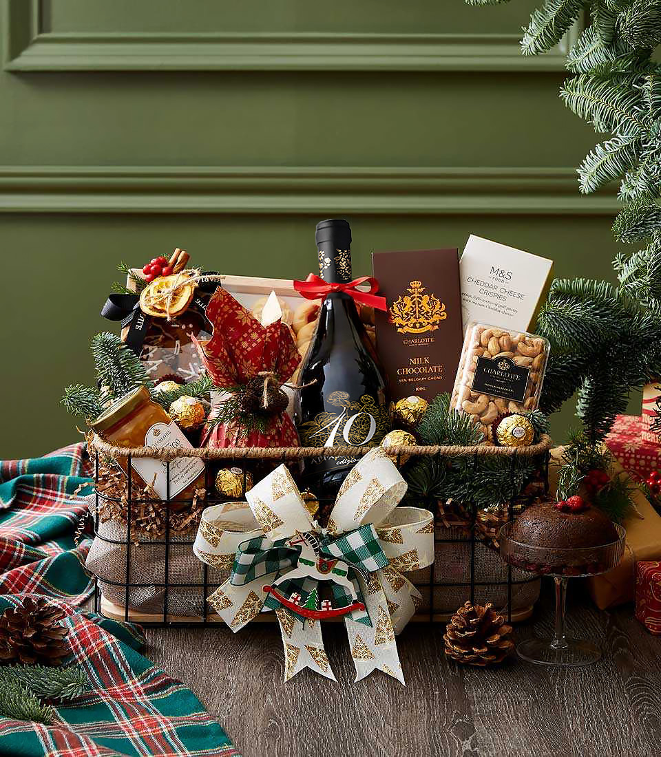 Rustic metal basket with red wine, cookies, nuts, chocolates, jam, and white-green Christmas bow