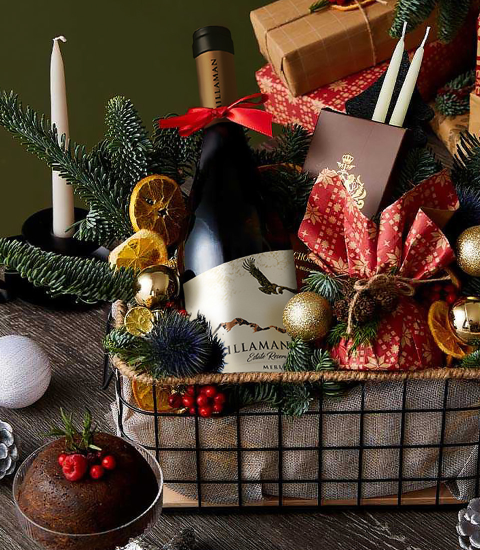 Festive Christmas basket with Millaman wine, red gift wrap, chocolate bar, candles, dried citrus, and holiday pine decorations