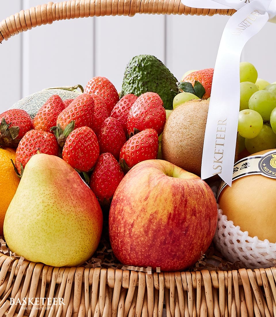 Indulge in the luxurious charm of our Classic Fresh Fruit Basket by BASKETEER. This elegant wicker basket overflows with a vibrant selection of nature's finest fruits—juicy strawberries, succulent grapes, a crisp apple, a ripe pear, creamy avocado, exotic kiwifruit, and a perfectly wrapped melon. The scene is adorned with a sophisticated white ribbon tied gracefully on the handle, showcasing the distinguished BASKETEER logo. A lavish treat that invites you to savor every moment.