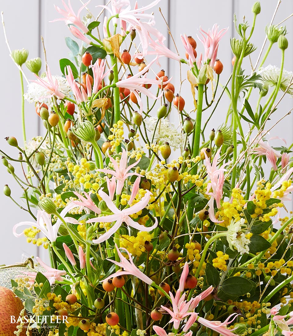 A lavish and enchanting bouquet featuring a medley of delicate pink blossoms, radiant clusters of small red berries, and sprigs of vibrant yellow flowers, all elegantly intertwined with lush green foliage. This opulent arrangement evokes the splendor of a Bright Fruit Flower Basket and is set against a sophisticated light gray paneled backdrop. The prestigious 