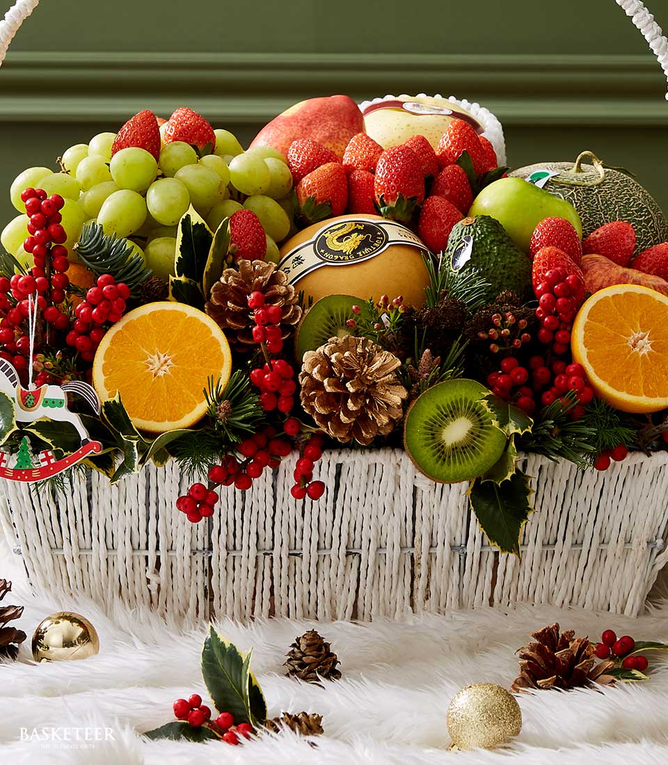 The opulent Premium Fruits Greetings Basket by Basketeer is an artisanal wicker masterpiece, brimming with a delectable variety of handpicked fresh fruits including succulent grapes, crisp apples, luscious strawberries, vibrant kiwis, and zesty oranges. Elegantly accented with pinecones, holly sprigs, and festive red berries, this exquisite arrangement is crowned with a dazzling gold ornament set against a lush green backdrop. A Basketeer ribbon graces the ensemble with understated luxury.