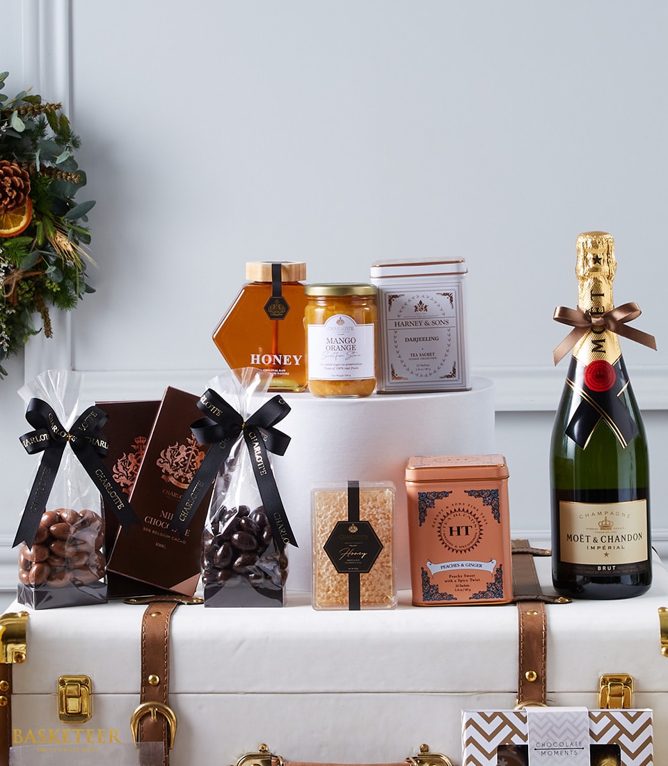 Immerse yourself in opulence with the Basketeer’s Wine Connoisseur's Gourmet Elegance gift basket. This exquisite collection features a bottle of Moët & Chandon champagne, luxurious jars of honey and mango chutney, a sophisticated tin of fine tea, decadent boxes of chocolates, an indulgent bag of chocolate-dipped coffee beans, and artisanal gourmet popcorn. Each meticulously curated item is gracefully arranged with festive embellishments and adorned with a signature ribbon bearing the Basketeer logo, creating a visually stunning display that invites you to savor every moment.