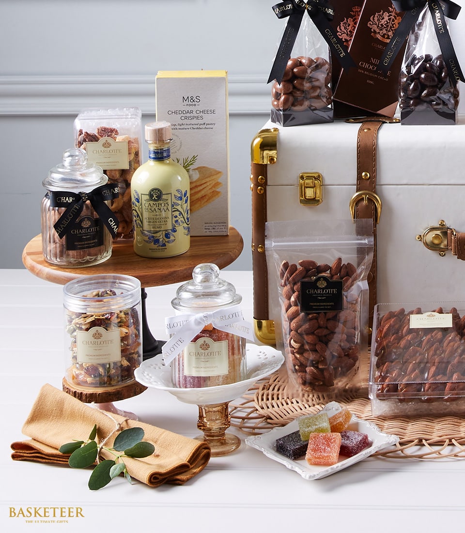Basketeer's Exquisite Wine Connoisseur's Gourmet Elegance: An opulent display of premium gourmet delights, featuring artisanal jars of nuts, sumptuous dried fruits, a luxurious bottle of virgin olive oil, delectable cheddar cheese crispies, and an indulgent assortment of chocolate-covered confections. Each item artistically arranged within a sophisticated picnic basket adorned with soft golden napkins. A discreet yet elegant ribbon bearing the Basketeer logo adds an extra touch of refinement to this inviting scene.