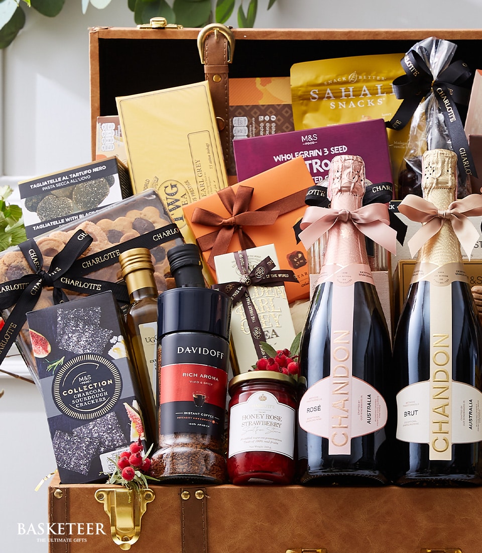 An opulent gift hamper brimming with a selection of gourmet delights, including bottles of Chandon champagne, an assortment of decadent chocolates, artisanal coffee, gourmet crackers, tempting snacks, and exquisite preserves. This sumptuous Luxury Wine Treats Gift Hamper is elegantly presented in a sophisticated brown trunk that proudly features the distinguished 