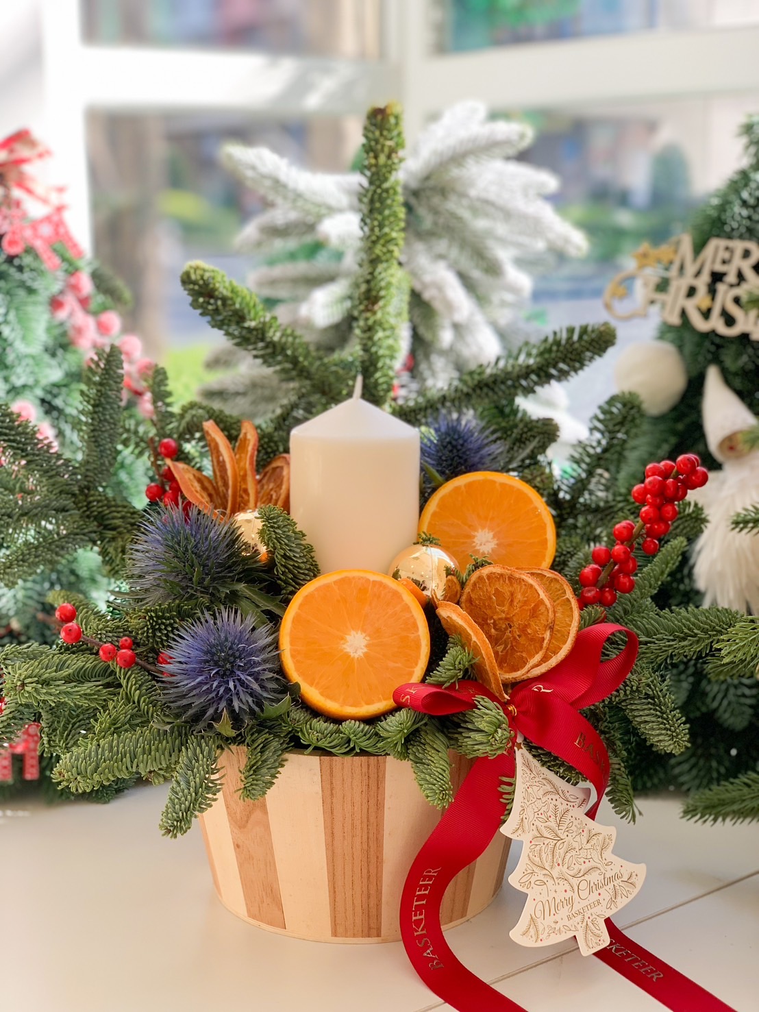 Holiday centerpiece with a white candle, pine branches, dried citrus slices, and festive accents.