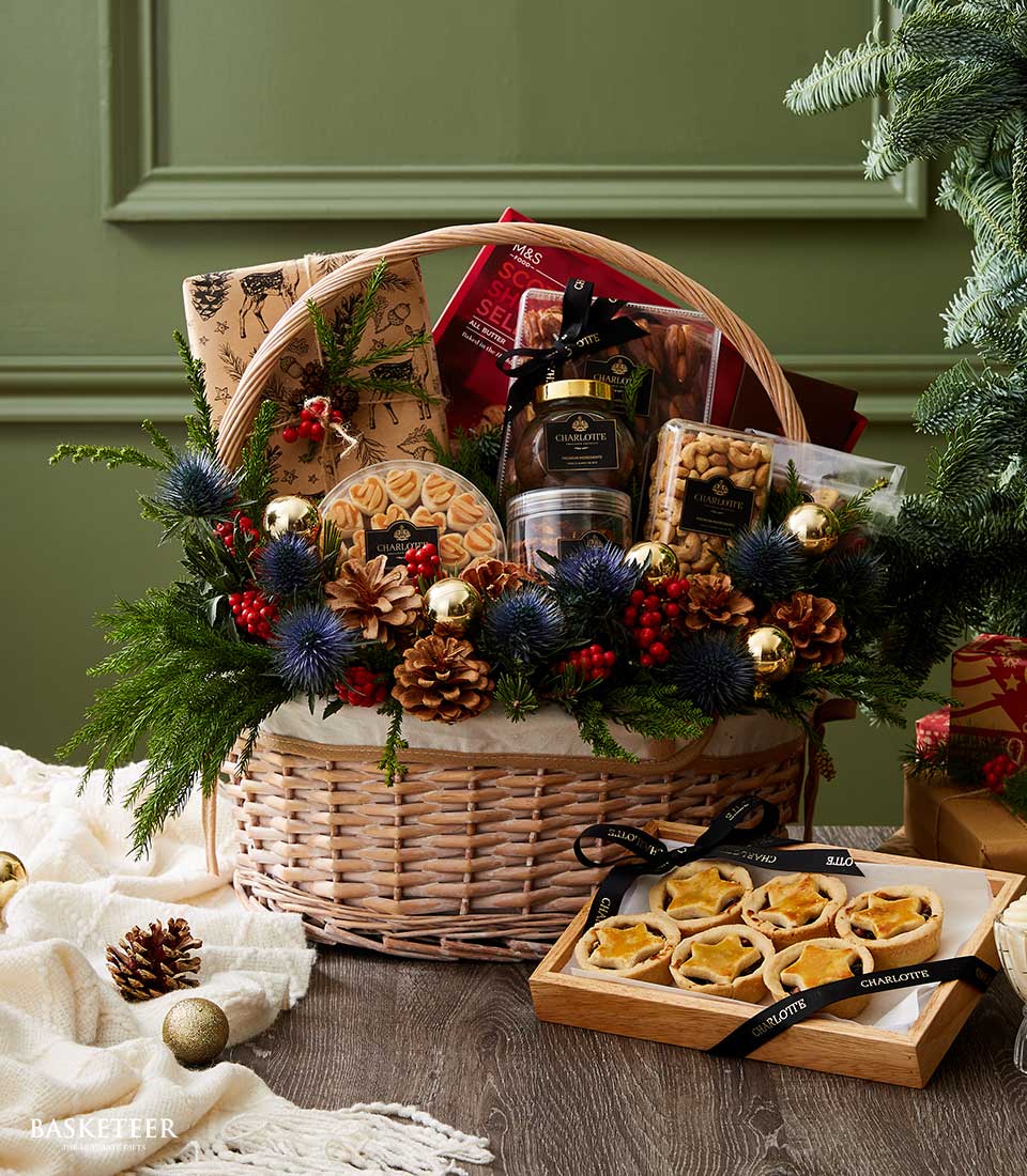 Festive wicker basket filled with cashews, cookies, gourmet treats, and adorned with greenery, pinecones, and holiday ornaments.