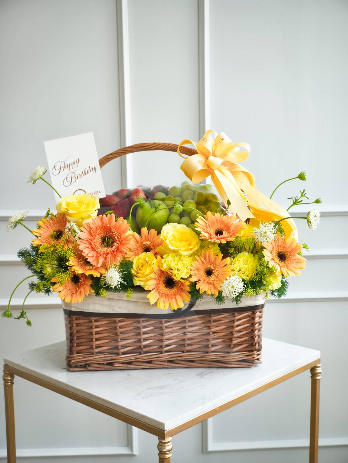 Premium fruit basket with yellow roses and orange gerbera flowers, decorated with a yellow ribbon, perfect for birthday or gift delivery in Bangkok