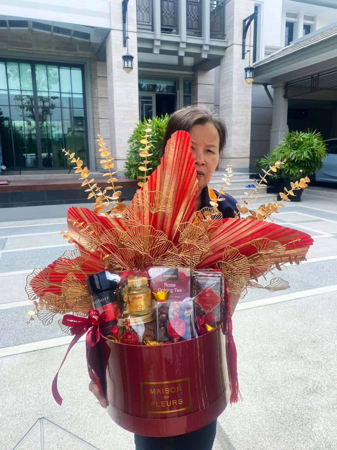 A person is holding a large, red floral arrangement gift basket labeled 