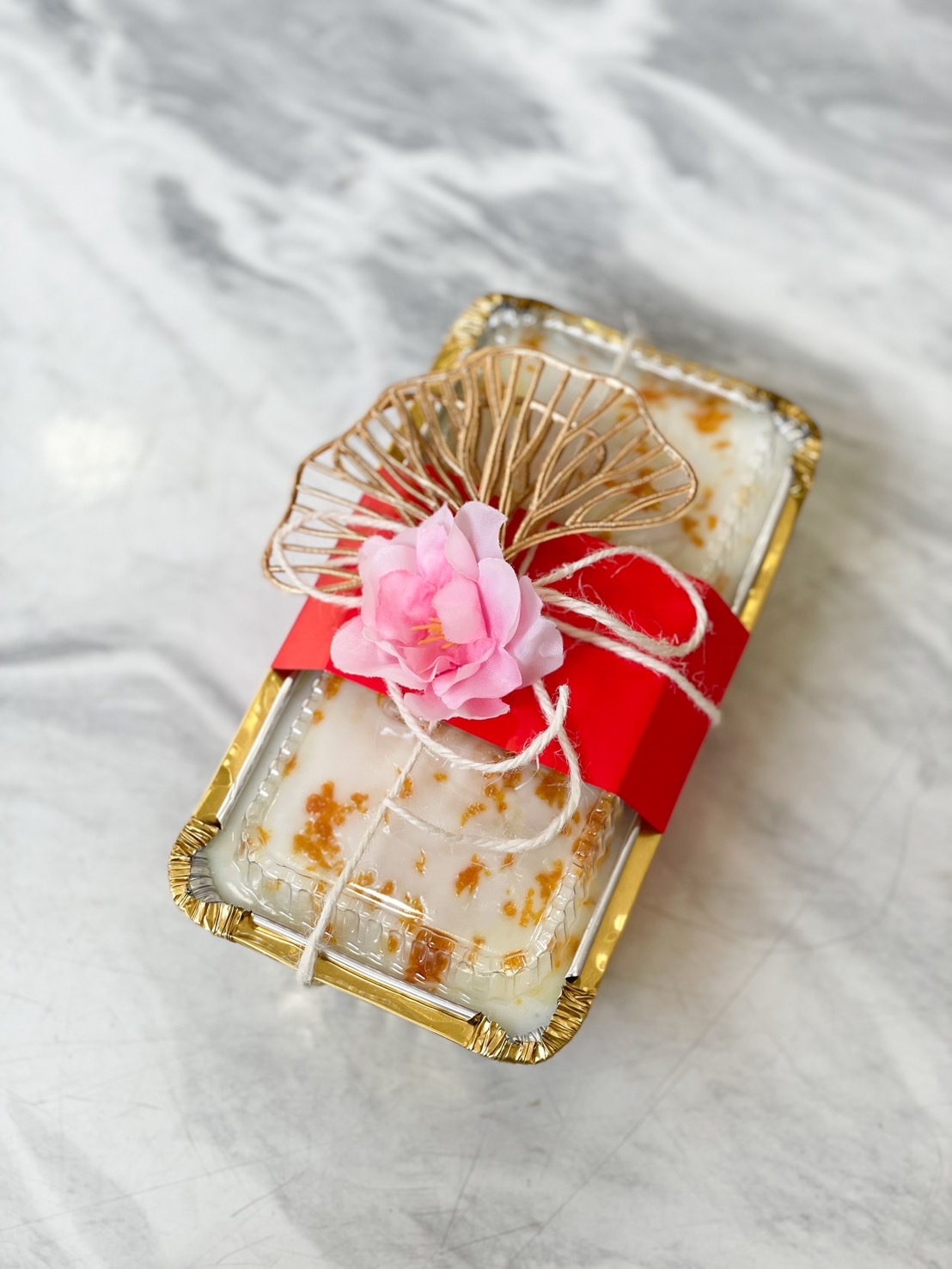 Mandarin zest pound cake in a gold tray, wrapped with a red ribbon and adorned with a pink flower decoration.