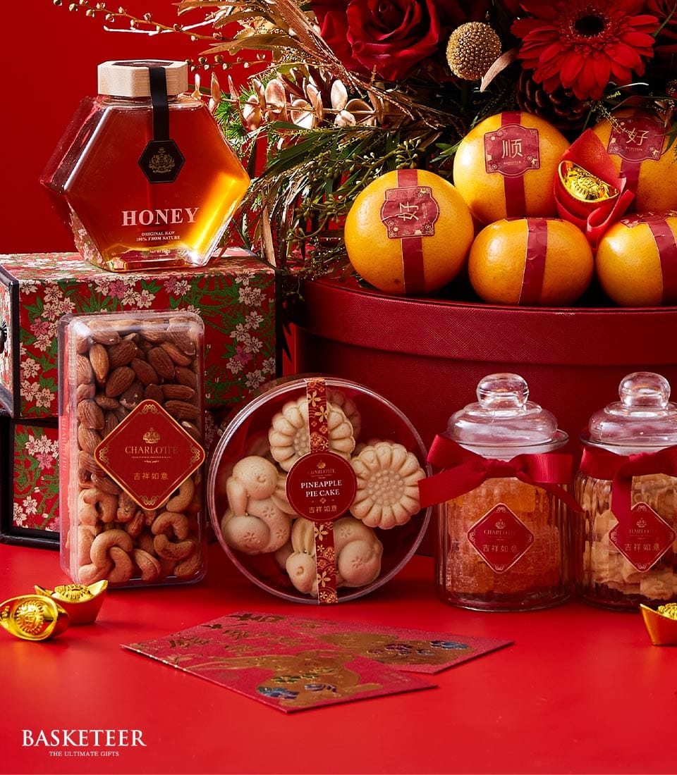 A lavish array of indulgent gifts featuring a jar of golden honey, an exquisite Basketeer box bursting with assorted gourmet nuts, luxurious pineapple cakes, decadent cookies, and artisanal jars of preserved fruits. Nestled within is an opulent basket brimming with succulent oranges. Red envelopes and shimmering golden ingots add to the splendor, all exquisitely adorned in rich red and gold decorations that evoke pure celebratory elegance. The prominent Basketeer logo on the ribbon and packaging elevates this display to a new level of sophistication.