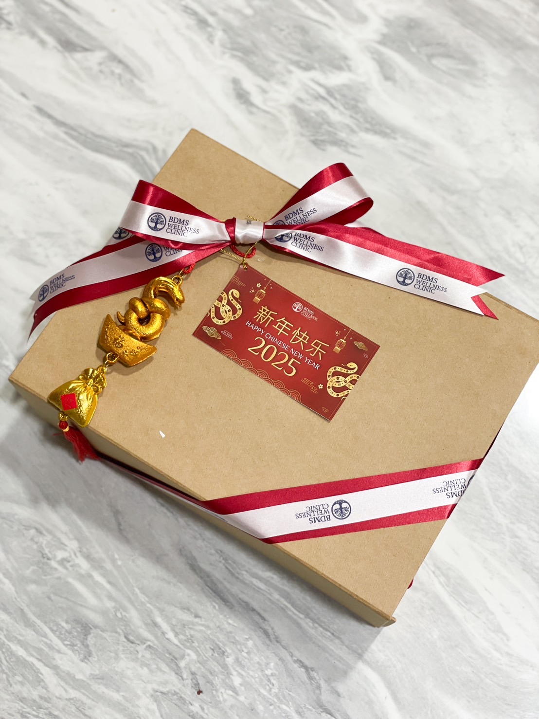 A kraft gift box tied with branded red and white ribbons, featuring a festive 