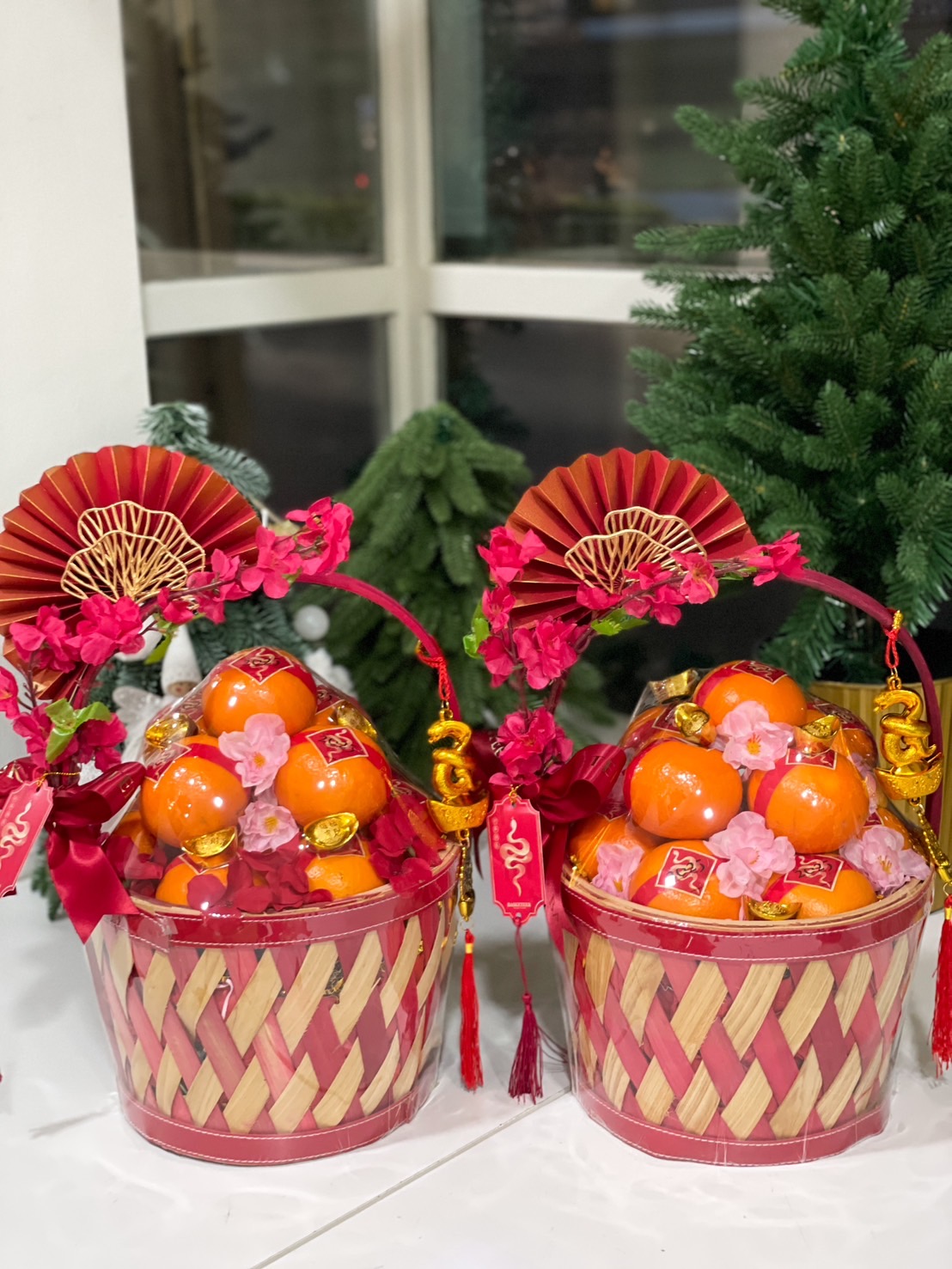 Traditional Chinese New Year gift basket filled with mandarin oranges, decorated with red and gold accents, pink blossoms, and festive charms for a touch of prosperity.