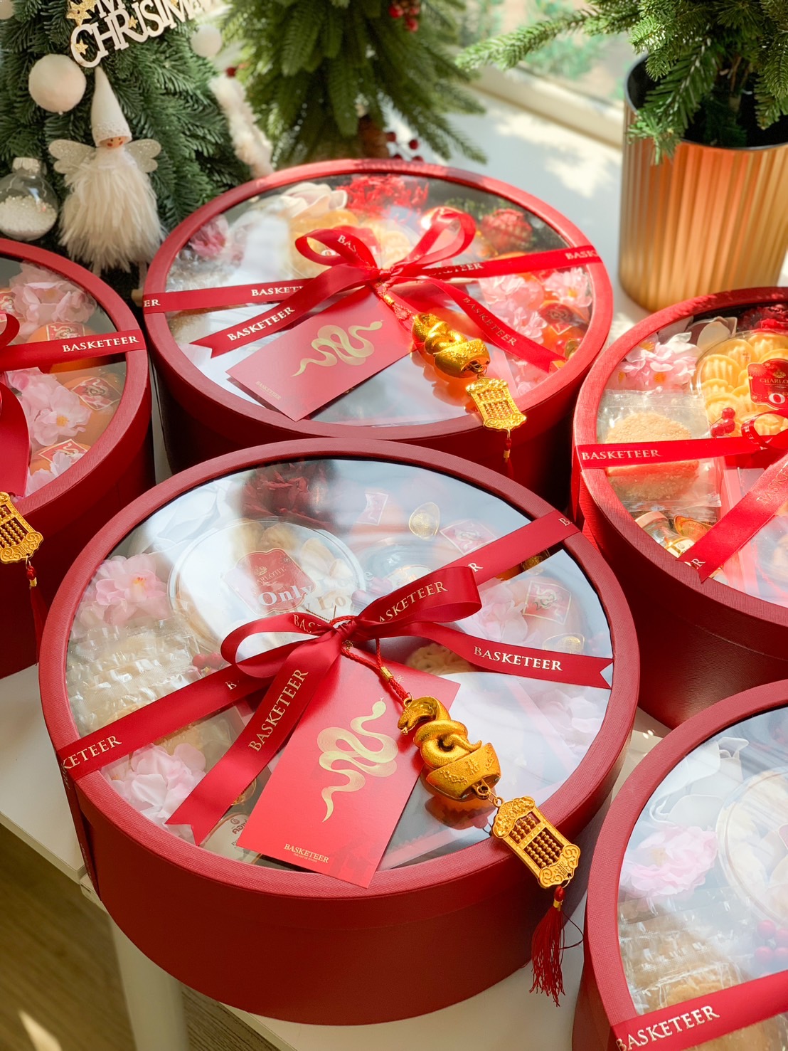 Elegant red round gift boxes with festive ribbons, golden charms, and an assortment of Chinese New Year treats.