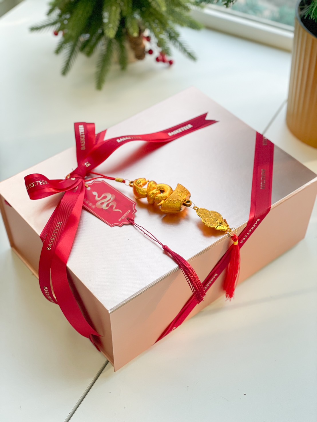 A rectangular beige gift box wrapped with a red ribbon that says 