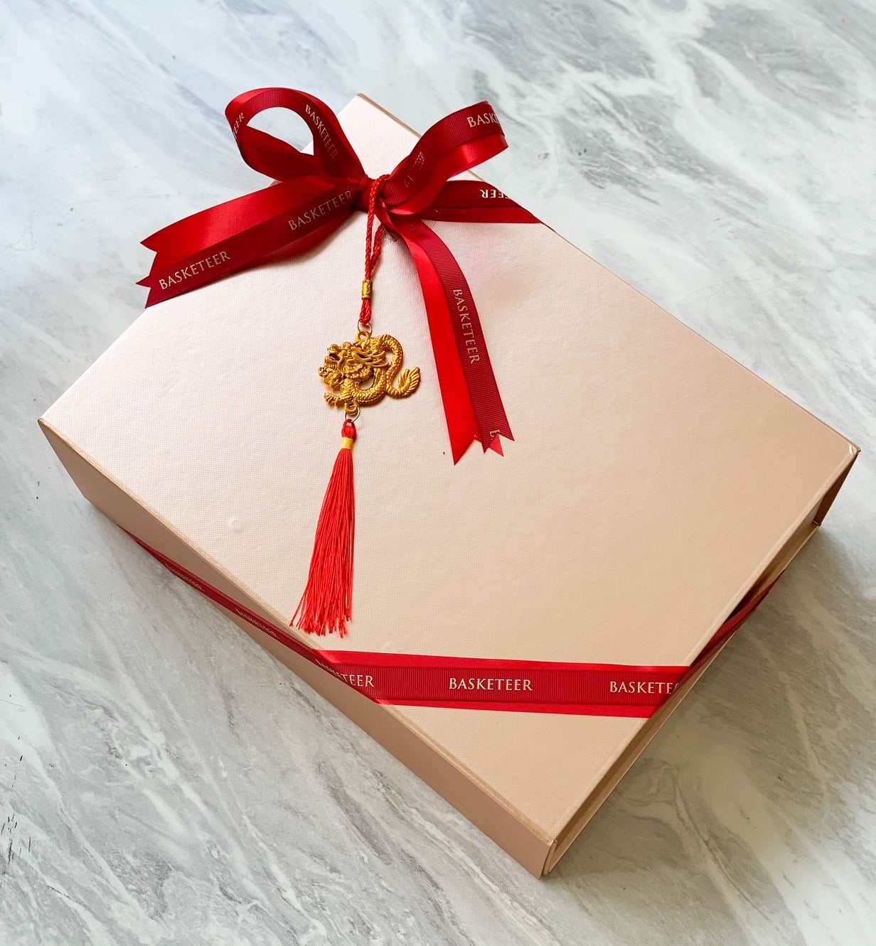 A rectangular beige gift box wrapped with a red ribbon that says 