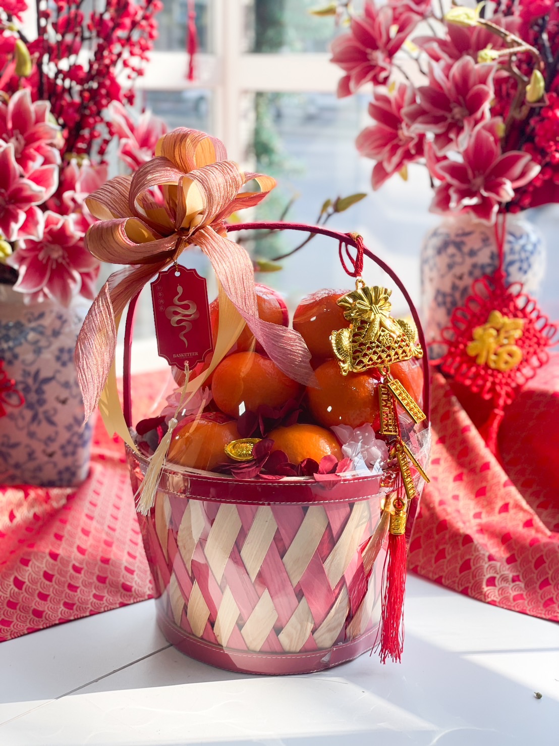 Chinese New Year prosperity fruit basket with fresh Mandarin oranges, a woven bamboo basket, gold charms, and festive decorations.