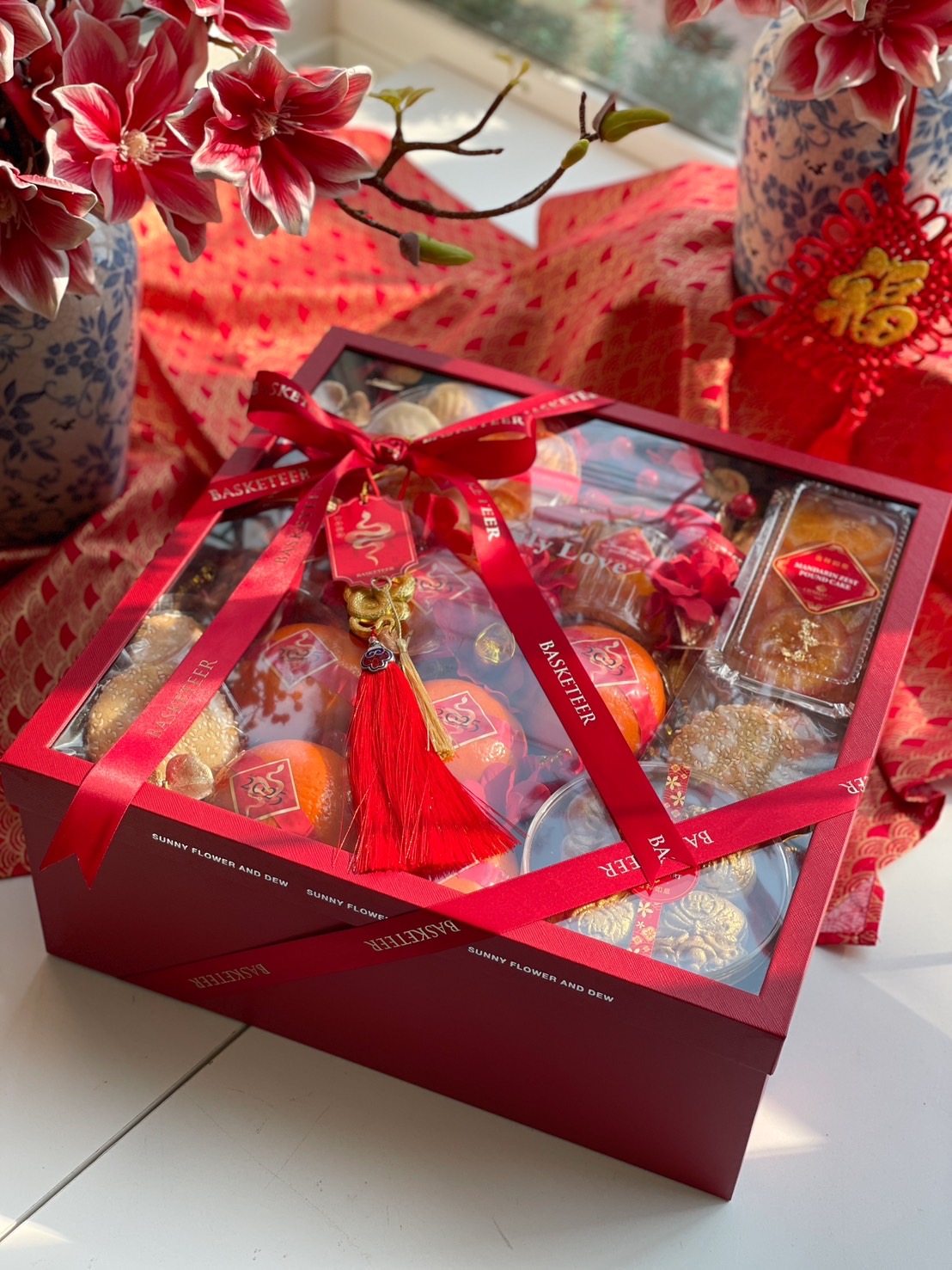 Premium Chinese New Year gift box with Mandarin oranges, festive sweets, and elegant red packaging adorned with lucky charms.
