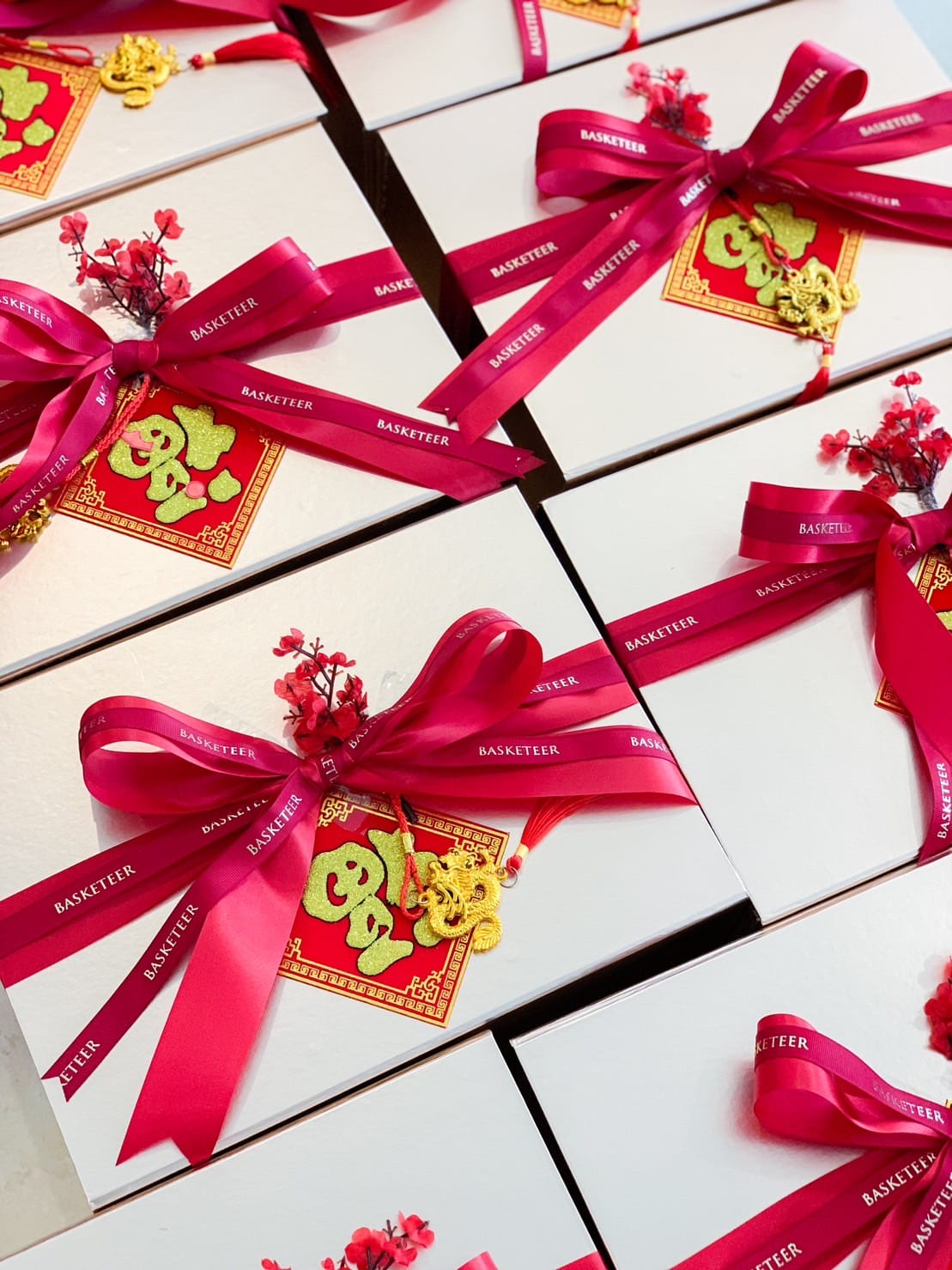 Several elegantly wrapped gifts are adorned with bright pink ribbons and golden ornaments featuring Chinese characters and symbols. Each package also includes a small flower embellishment, and the ribbons are labeled with 