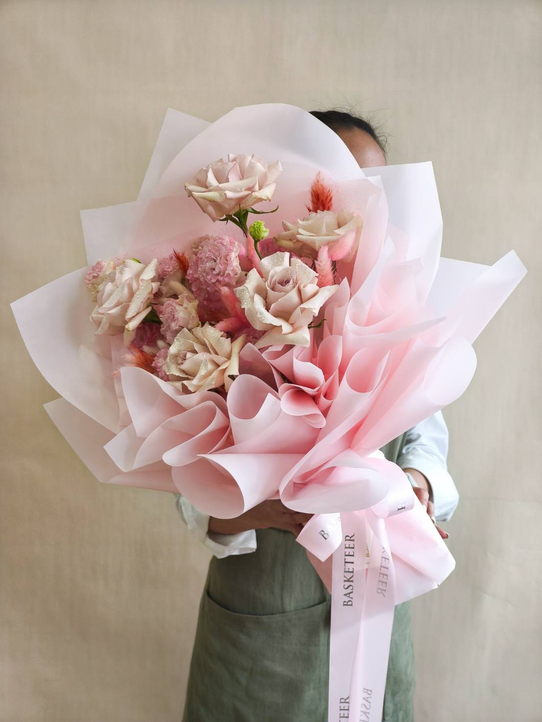 Luxury pastel pink bouquet with roses, carnations, and accent blooms, wrapped in soft pink paper with satin Basketeer ribbon.
