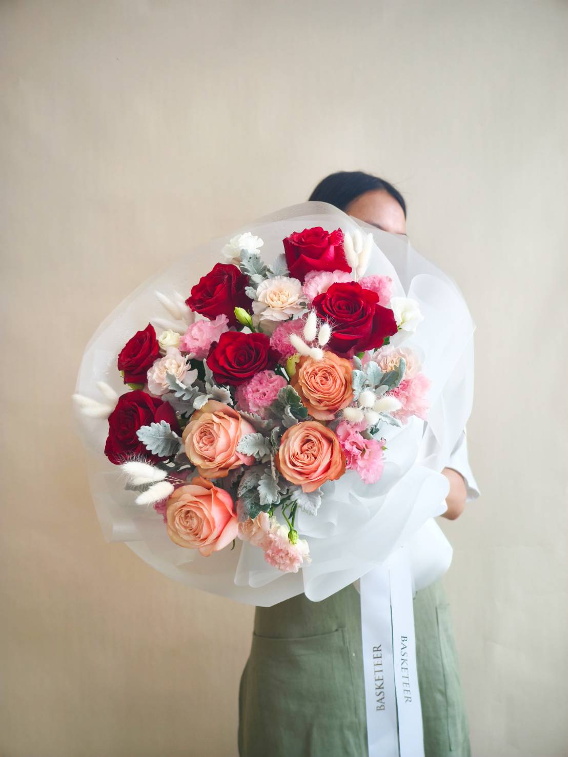 Elegant bouquet with red roses, peach roses, pink carnations, white fillers, and silver foliage wrapped in white paper.