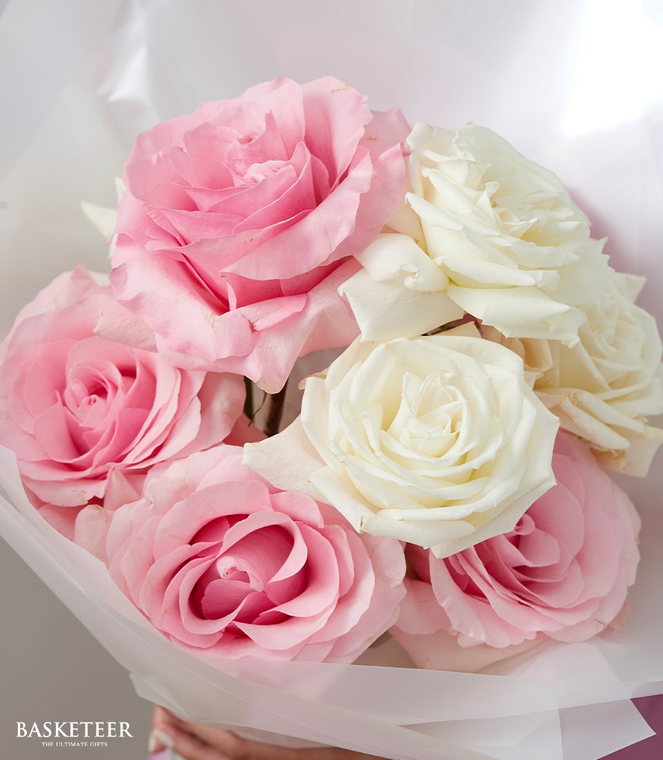 A sumptuous bouquet of pink and white roses, elegantly wrapped in pristine translucent white paper. The roses are fresh and vibrant, their soft, delicate petals exuding an air of timeless beauty. In the lower left corner, a glimpse of the prestigious 