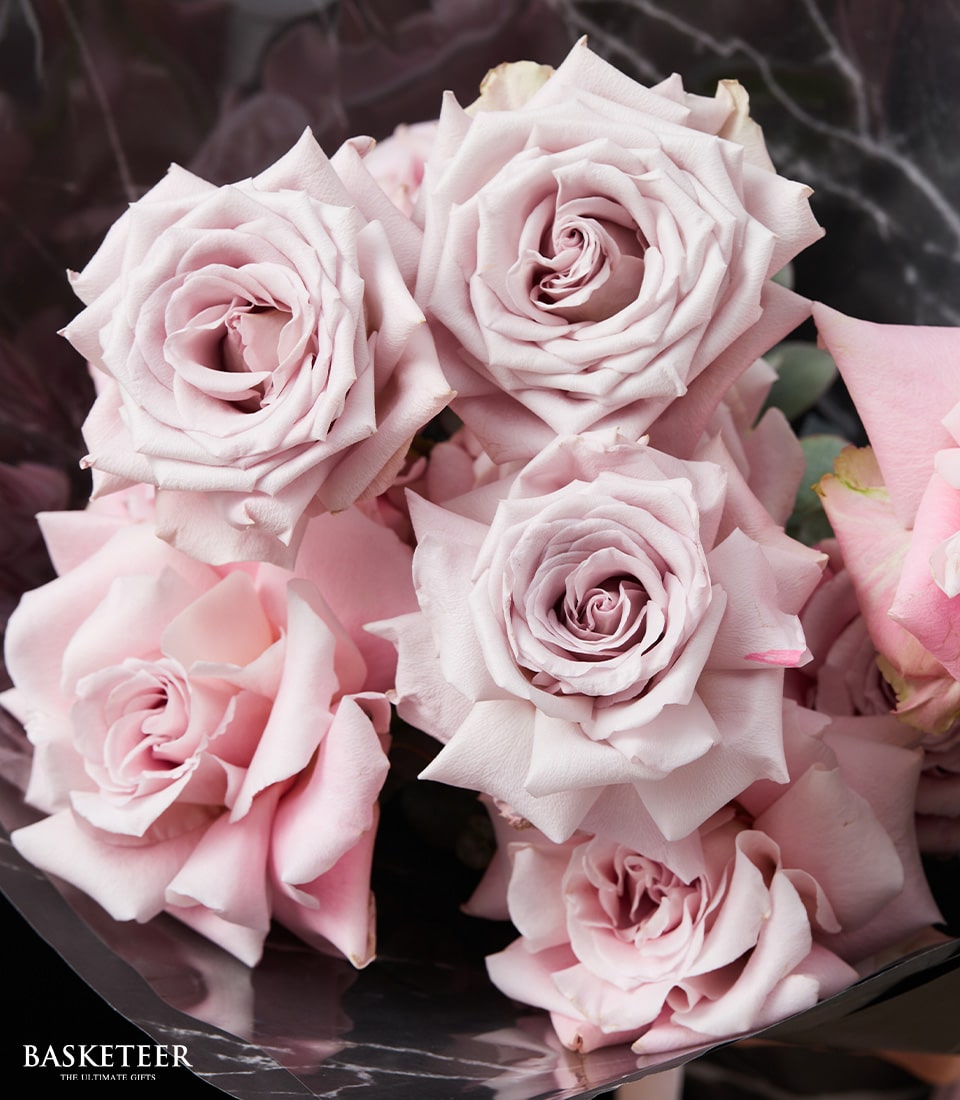 A luxurious close-up of a bouquet featuring six exquisite light pink roses in full bloom, their petals elegantly curled and emanating a timeless beauty against an opulent dark backdrop. In the bottom left corner, the prestigious brand name 