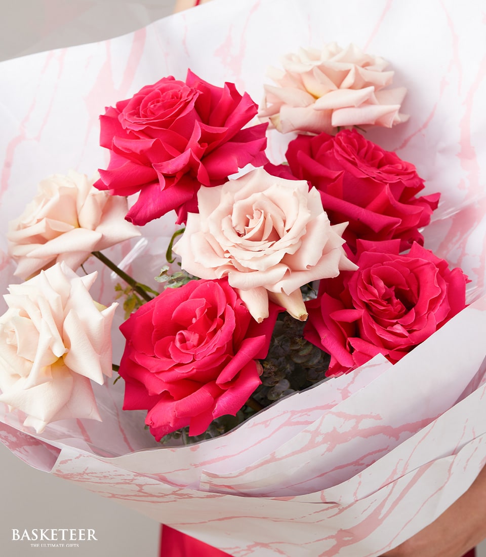 A lavish bouquet showcases an exquisite blend of radiant hot pink roses and delicate blush pink roses, elegantly wrapped in sophisticated white and pink marbled paper. The eye-catching creation is adorned with the distinguished 