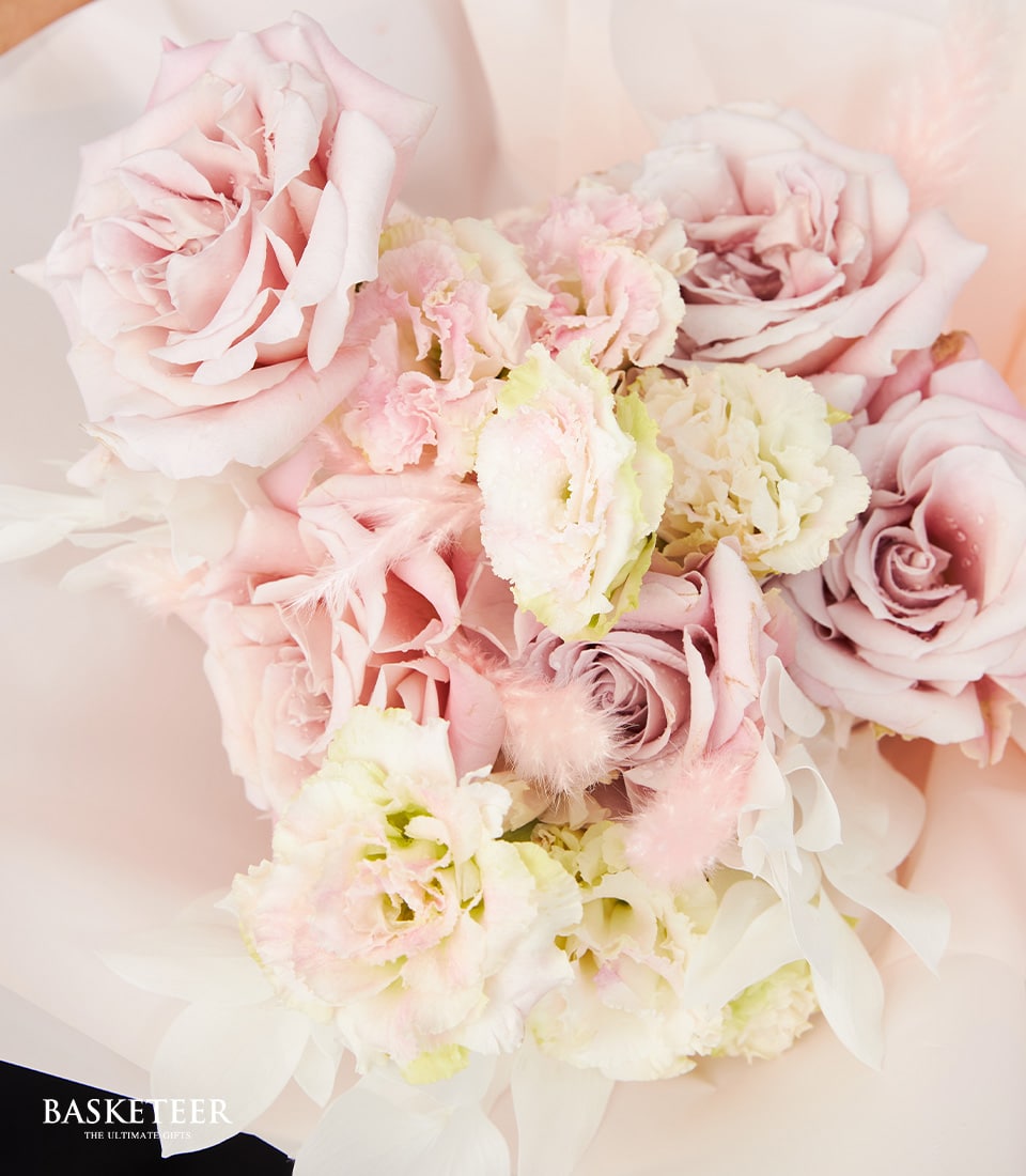 A close-up of a luxurious pastel-colored floral arrangement showcasing an exquisite medley of pink roses and other delicate blooms. The soft, slightly ruffled petals radiate romance and elegance, forming a stunning bouquet. The word 
