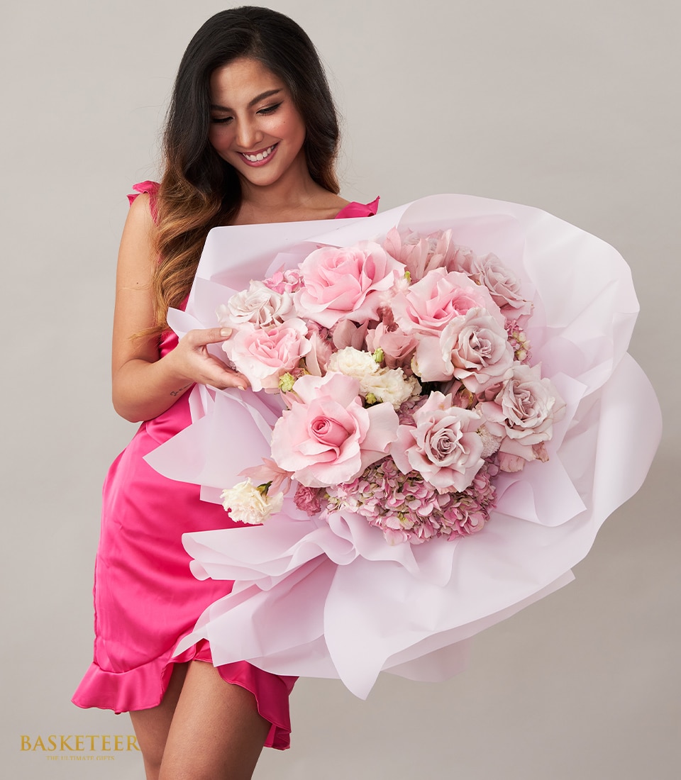 A radiant woman, elegantly dressed in a vibrant pink gown, gracefully holds an opulent bouquet of pink and white flowers, meticulously wrapped in delicate white paper. The minimalist light grey backdrop enhances the luxurious charm. At the bottom left corner, the prestigious 