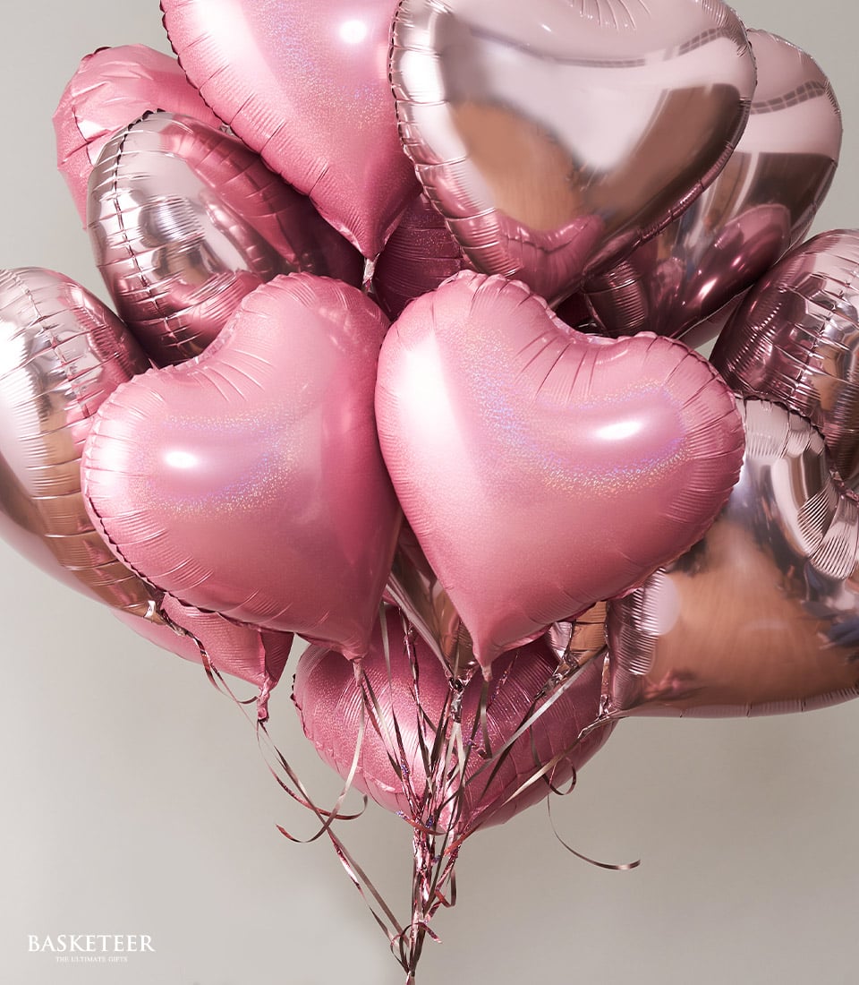 A lavish ensemble of heart-shaped metallic pink balloons elegantly tied together with delicate pink strings. These exquisite balloons float gracefully against a soft, light background, their gleaming surfaces capturing light to create enchanting reflections. The luxurious composition is accentuated by the 