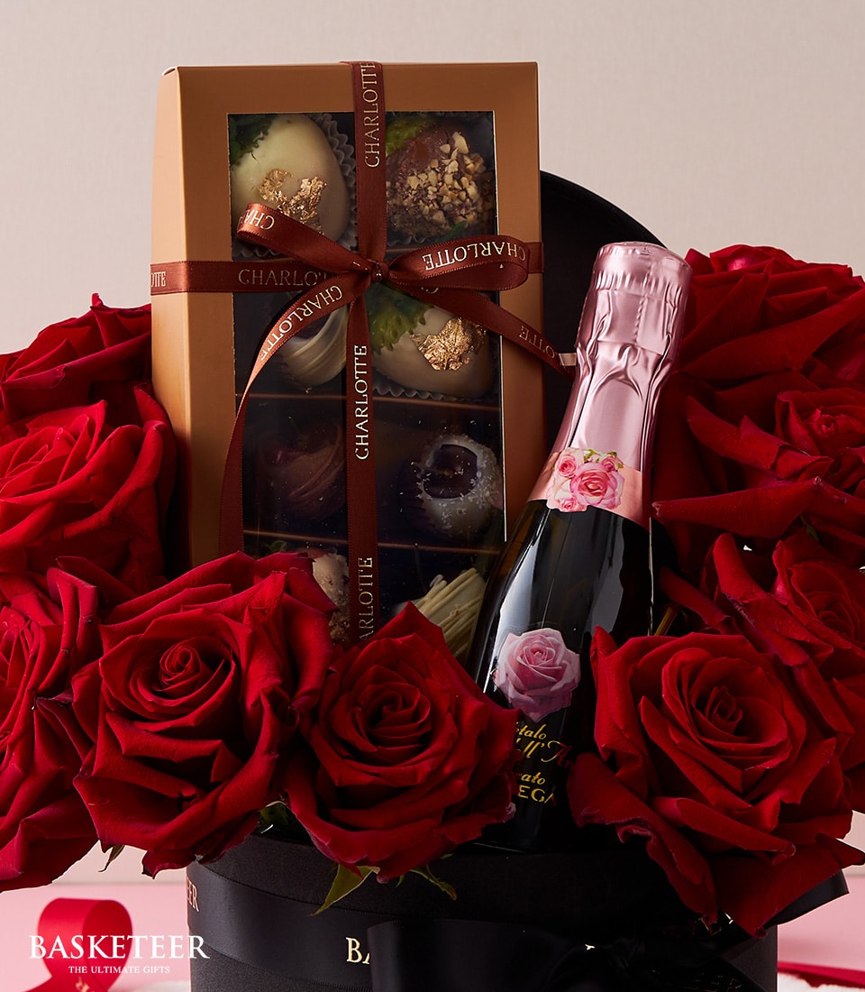 An exquisite gift set featuring a premium bottle of pink sparkling wine, an assortment of decadent chocolates, and a bouquet of vibrant red roses, all elegantly presented. The stunning items are arranged in an opulent black box adorned with the 