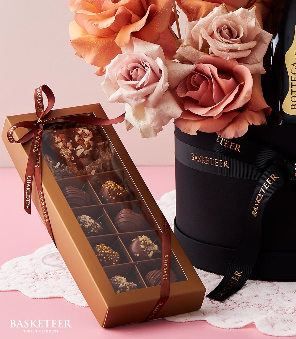 A luxurious Basketeer gift set artfully displayed to captivate the senses. The centerpiece is a sophisticated box of 12 impeccably assorted chocolates, showcased under a transparent lid and elegantly tied with a rich brown ribbon inscribed with 