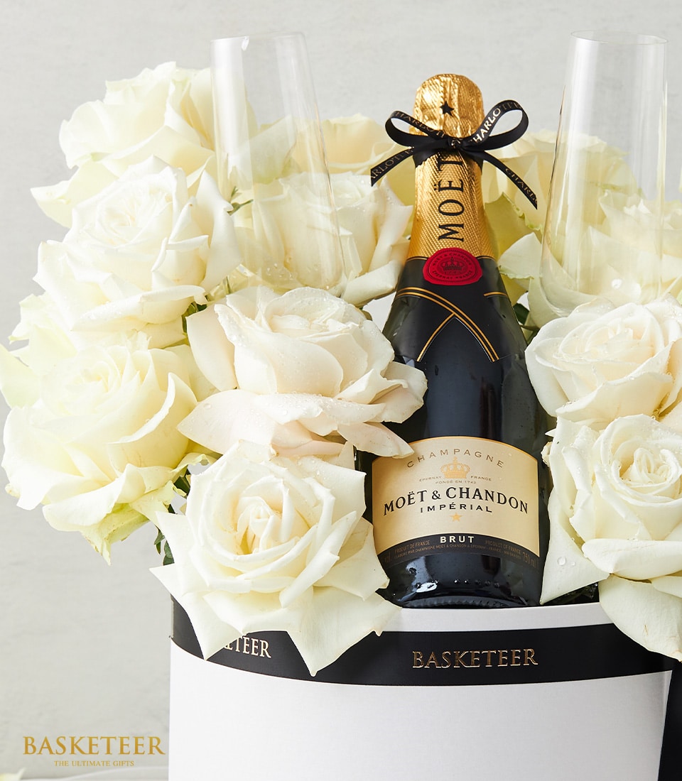 A lavish arrangement of pristine white roses and a bottle of Moët & Chandon champagne is beautifully presented in an exquisite white basket. The opulent display suggests it’s a luxurious gift from Basketeer, with their signature ribbon tastefully adorning the ensemble. Two elegant champagne flutes complete this inviting scene, perfect for celebrating life's finest moments.