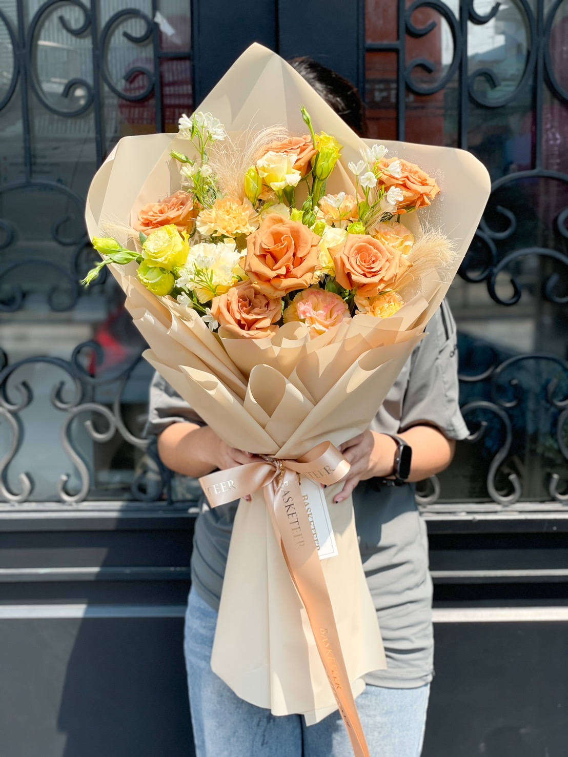 A luxurious bouquet of peach and yellow roses, elegantly wrapped in beige paper with a satin ribbon – the perfect floral gift for any occasion.