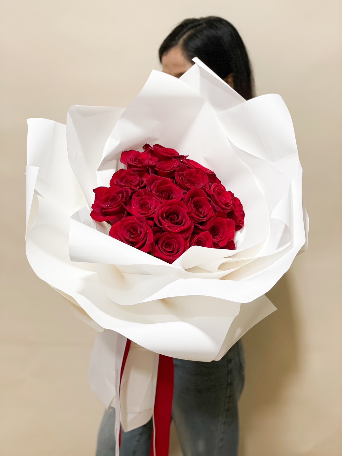 A stunning bouquet of red roses, elegantly wrapped in voluminous white paper with flowing ribbons for a sophisticated and romantic floral arrangement.