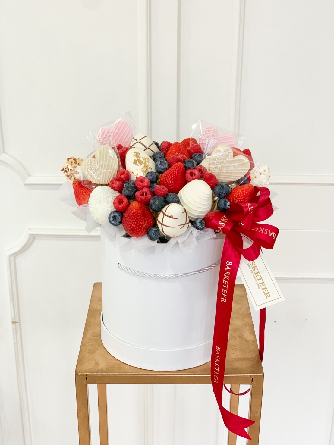 Gourmet fruit bouquet with chocolate-dipped strawberries, fresh raspberries, blueberries, and decorated heart-shaped treats in a white gift box.