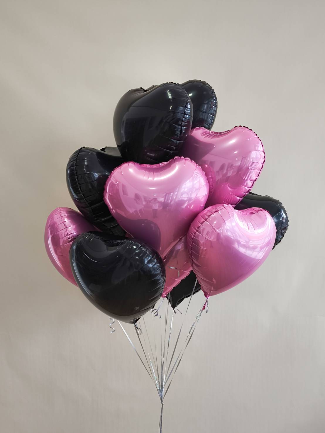 Heart-shaped foil balloon bouquet in black and pink tones, tied with silver strings