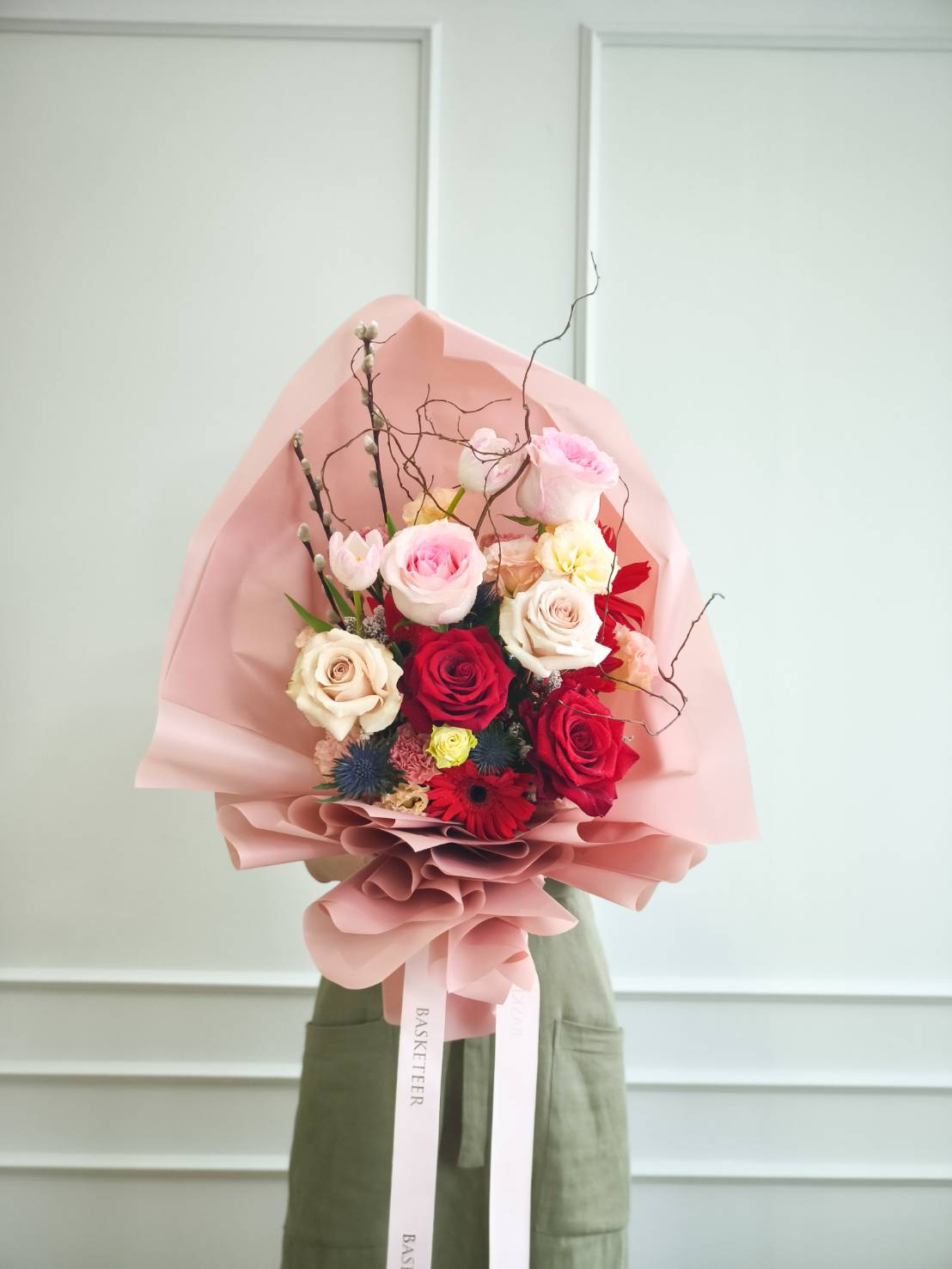 Romantic bouquet with red and pink roses, cream roses, tulips, gerberas, and accent fillers, wrapped in soft pink paper with ribbon