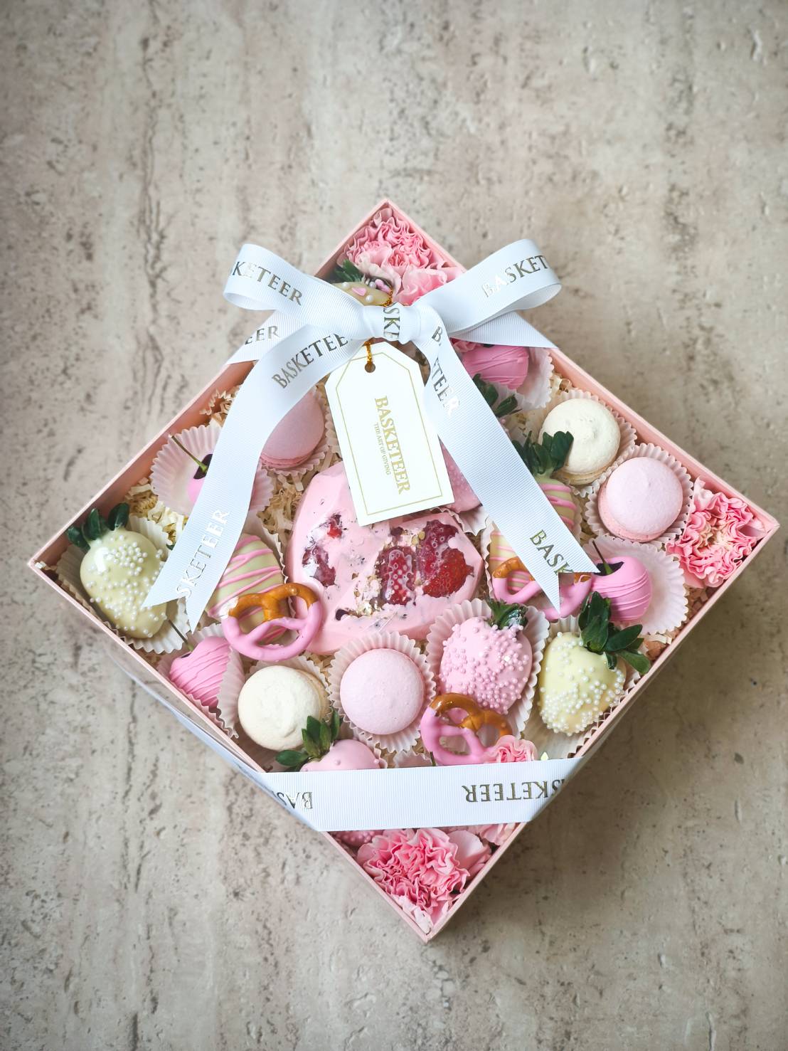Pink gift box with macarons, chocolate strawberries, pretzels, and flowers, tied with white satin ribbon – luxury sweet gift in Bangkok