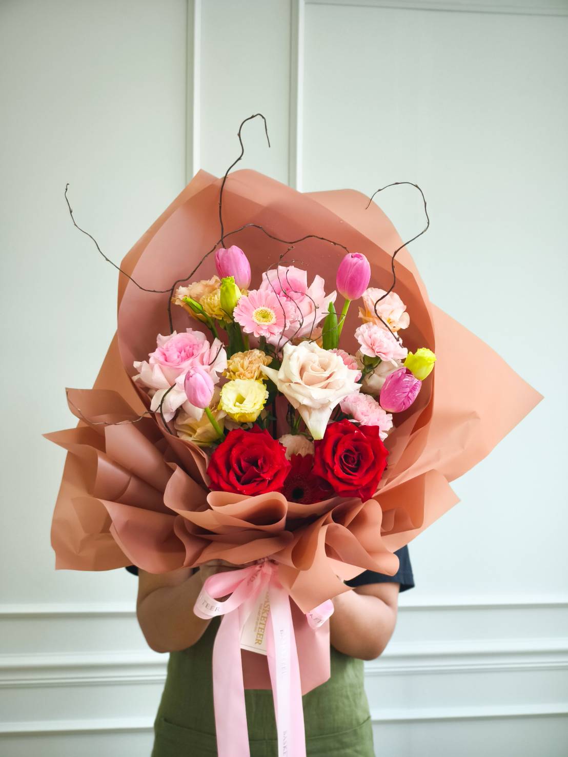 Bouquet with red roses, blush roses, pink tulips, gerberas, and mixed pastel flowers wrapped in peach paper
