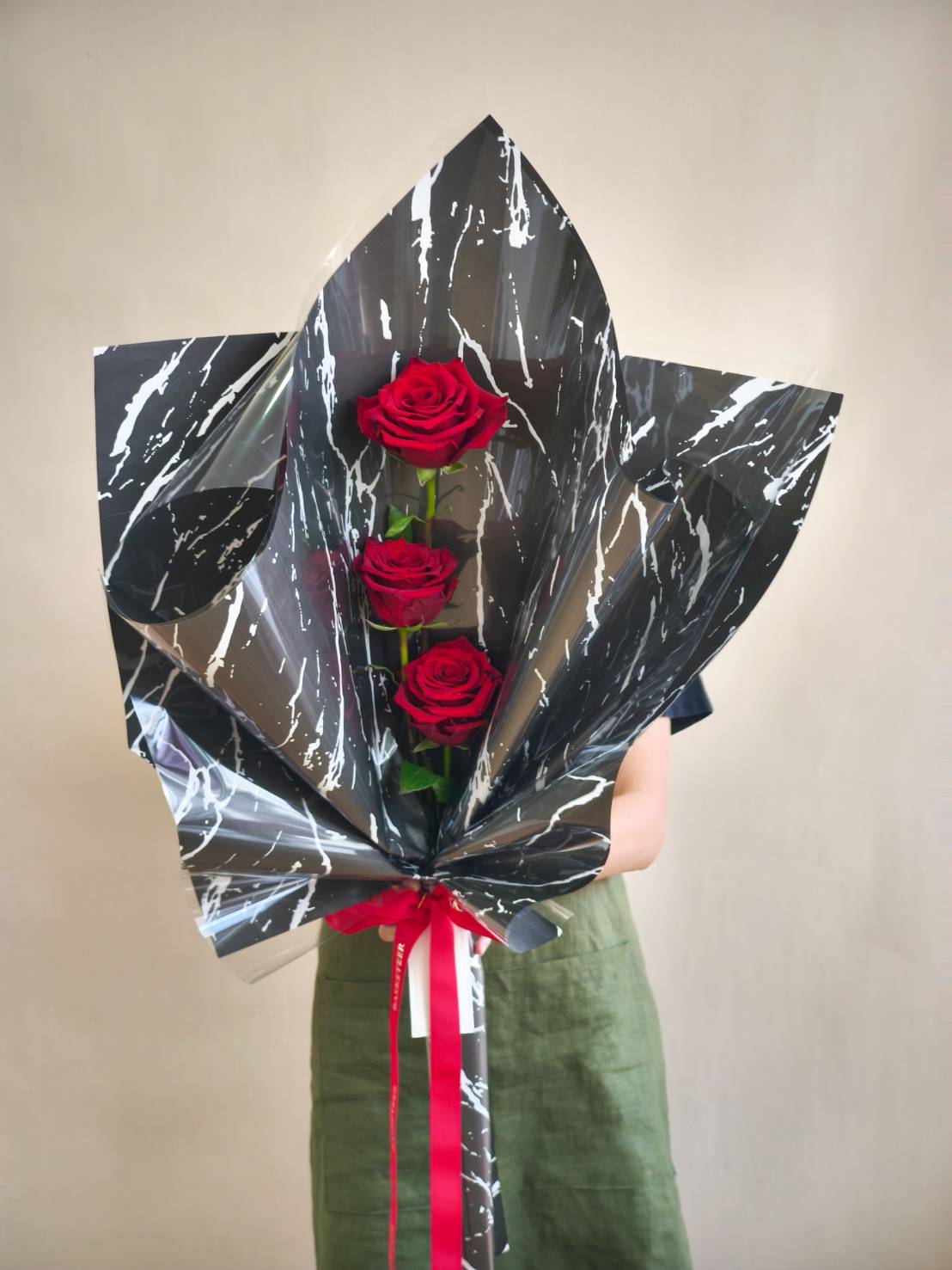 Elegant bouquet of three red roses wrapped in black marble-pattern paper with red ribbon.