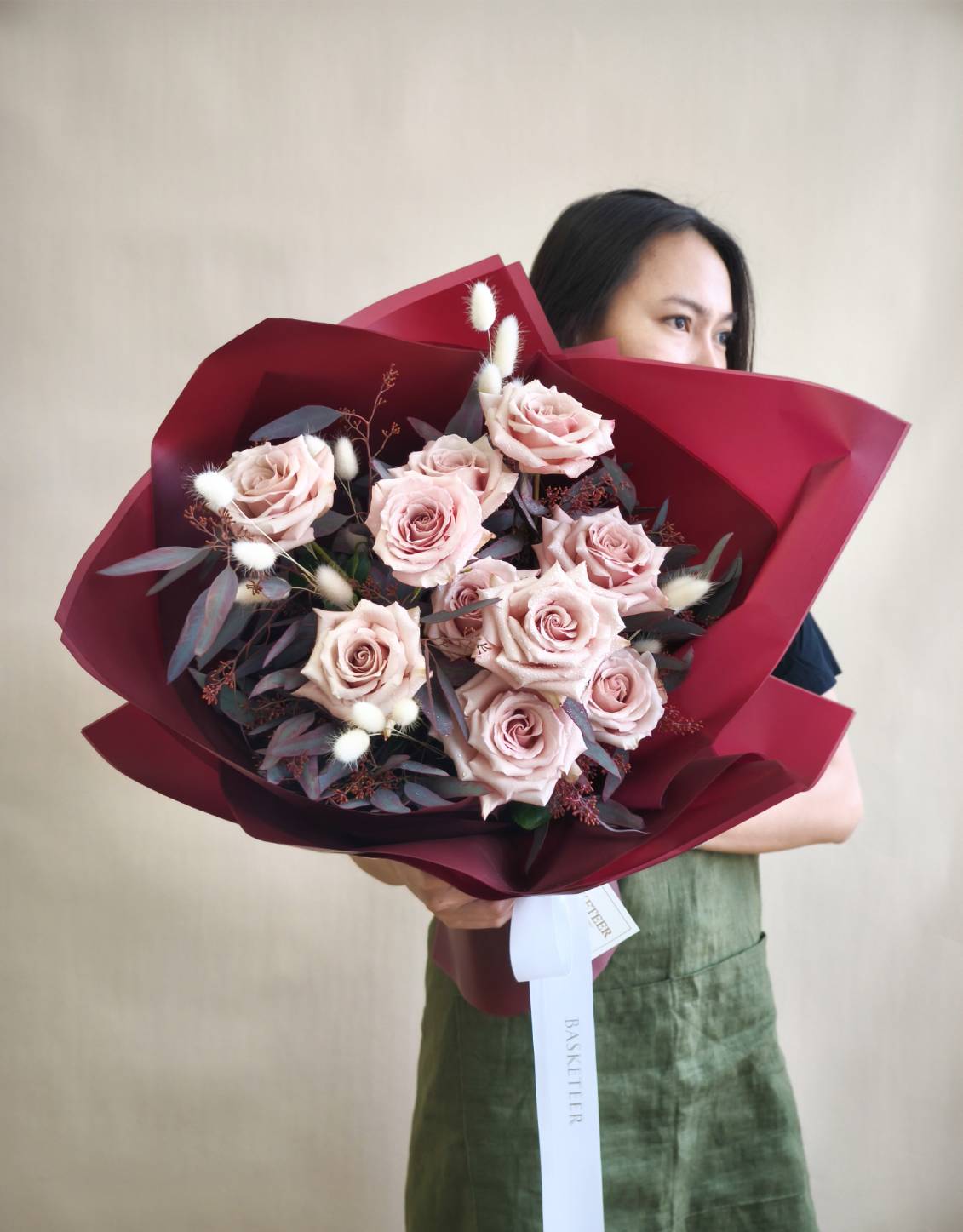 Luxurious bouquet of nude pink roses wrapped in deep red paper with white ribbon.